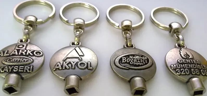 promosyon dört gümüş metal anahtarlık, üzerlerinde farklı firma adları baskılı, beyaz arka plan