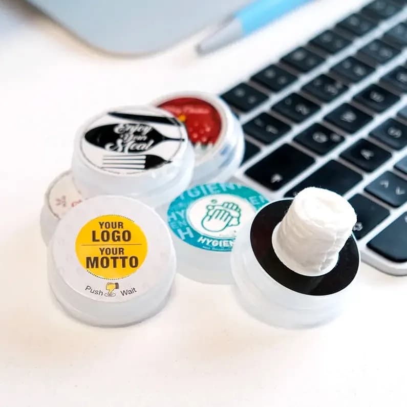 promosyon beyaz yuvarlak plastik kutular, biri mendilli, sarı ve mavi etiketli, klavye önünde