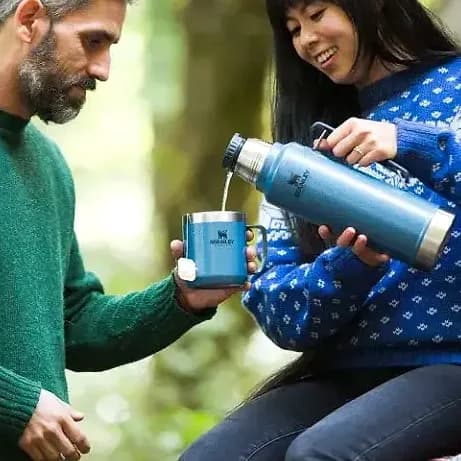 Promosyon mavi termos ve bardak, orman fonunda iki kişi arasında
