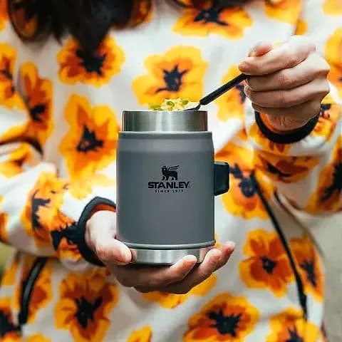Promosyon mat gri yemek termosu çiçekli polar giyen kişinin elinde, yemek yerken