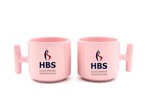 İki pastel pembe promosyon latte fincanı, koyu mavi firma ve organizasyon baskısı