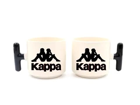 İki beyaz promosyon latte fincanı; siyah kulplu, spor markası logo baskılı
